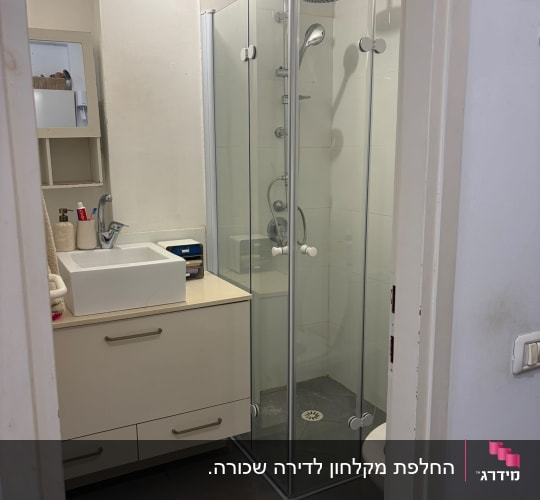 מקלחון פינתי שקוף מותקן בחדר רחצה לצד ארון כיור